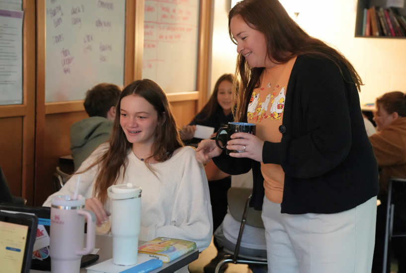 teacher helps a student on their laptop in English class